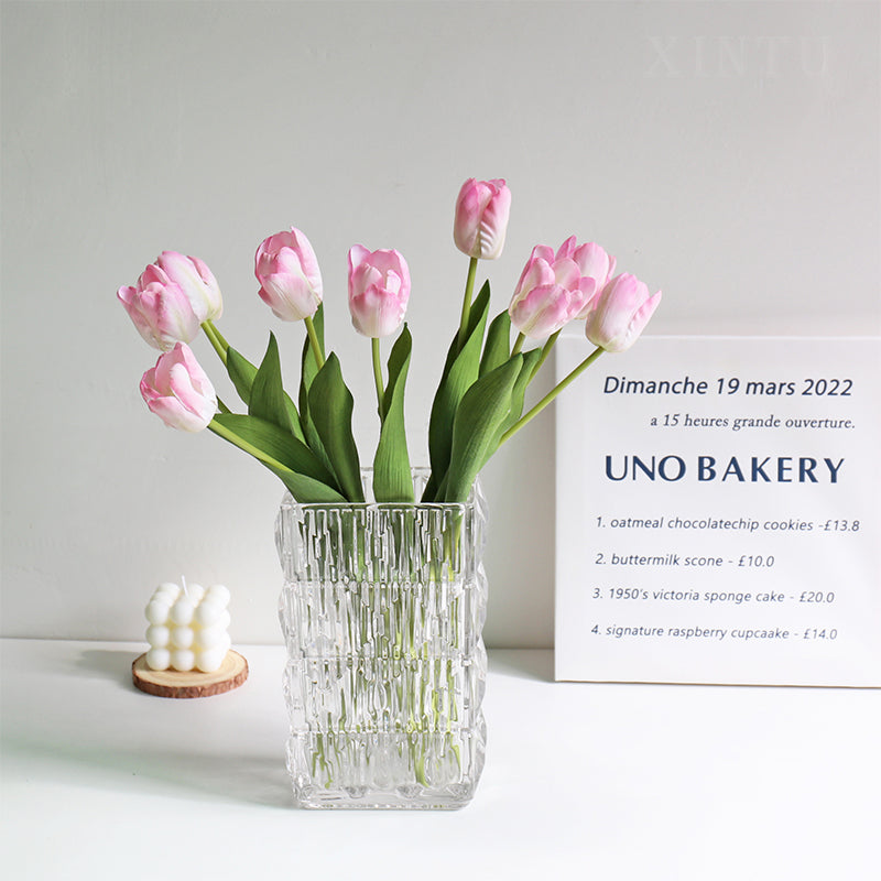 Pink faux tulips with green leaves in a textured square glass vase