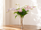 Pink, white and lilac faux begonia stems arching over a clear glass vase