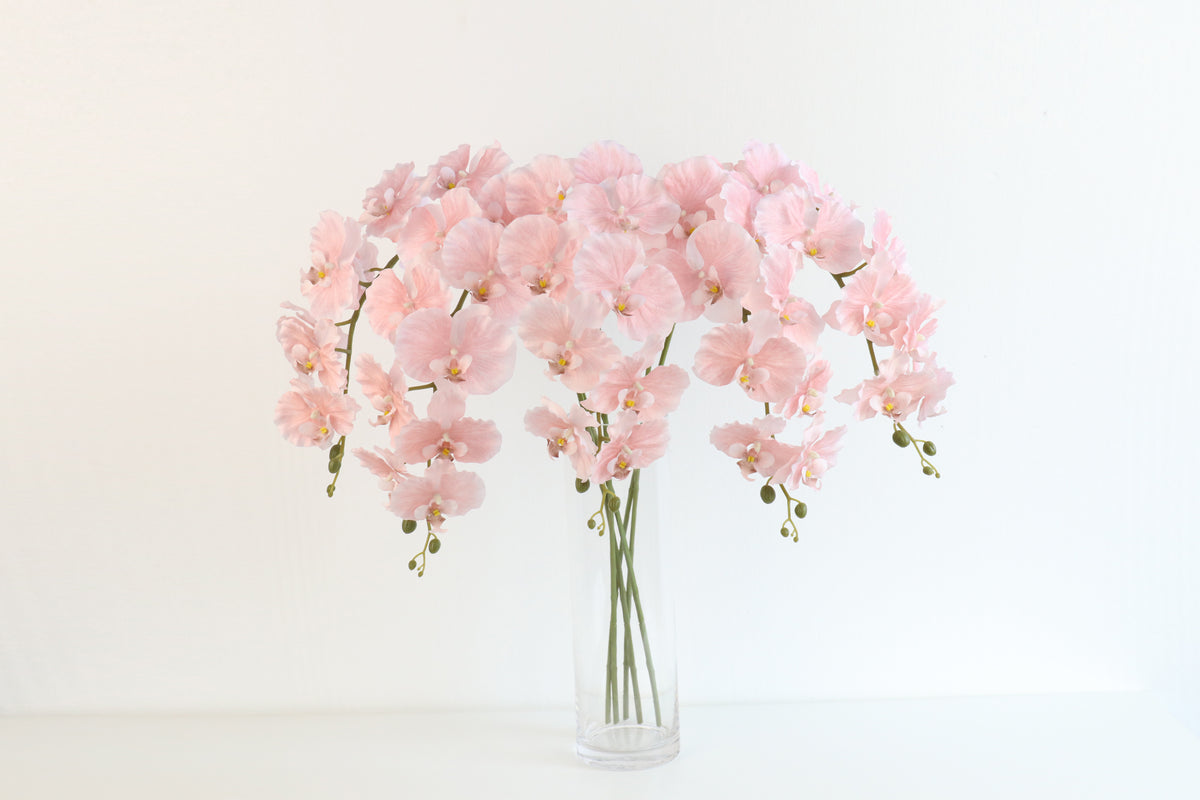Long-stem faux pink butterfly orchids fanning wide from a tall glass vase