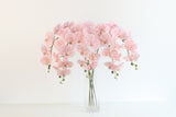 Long-stem faux pink butterfly orchids fanning wide from a tall glass vase