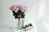 Pale pink faux rose stems arranged in a fluted glass vase in soft daylight