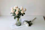 Cream faux roses in a green glass jar with two white stems laid beside