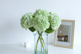 Green faux hydrangeas styled in a blue glass vase