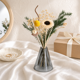 Cream sunflower with yellow craspedia and pine in a grey glass vase