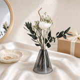Small dried arrangement with a white bloom and eucalyptus in a grey glass vase