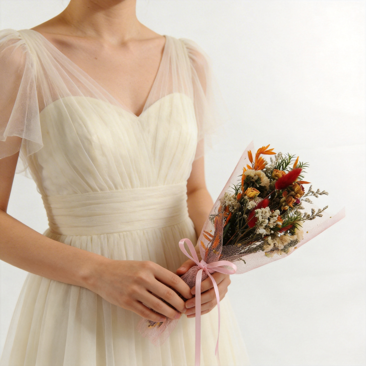 Orange and rust dried bouquet wrapped in pink tulle, held at the side